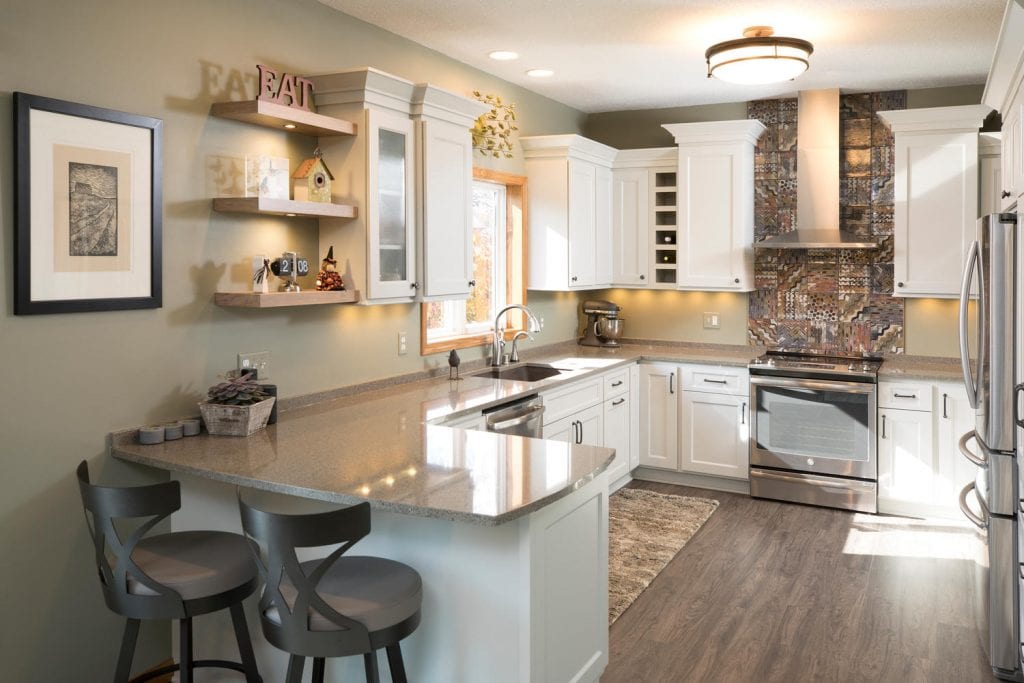 a kitchen with natural lighting, white cabinets and gray countertops. there's also a backsplash with a distinctive, rustic pattern.