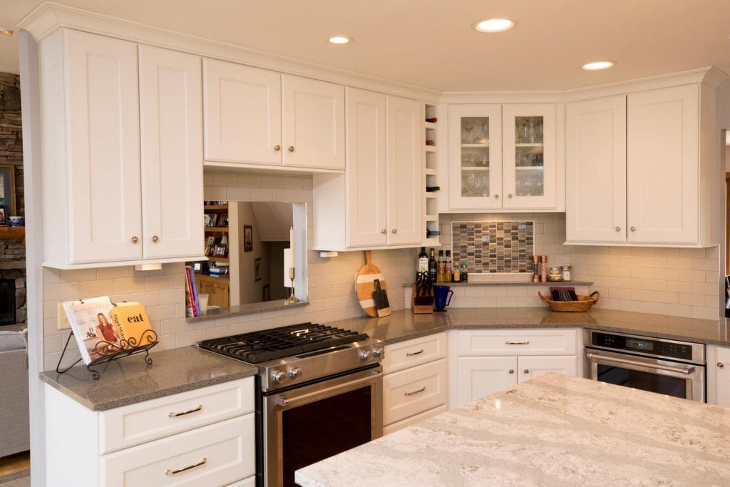 a kitchen with white cabinets and gray countertops, showcasing a serving hatch