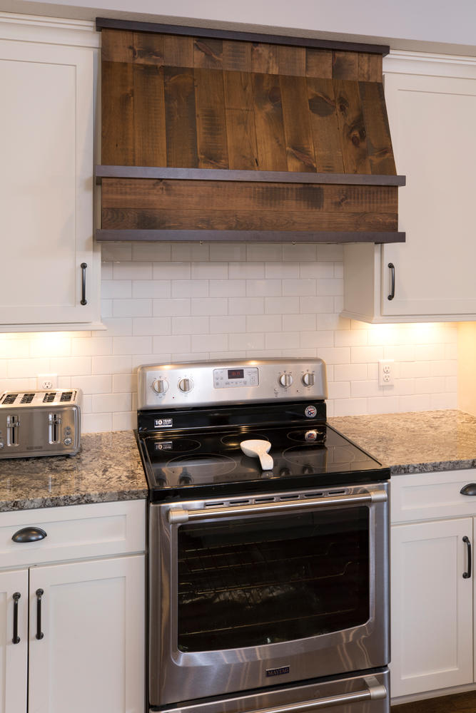 a stove with a rustic hood, surrounded by white cabinets and gray countertops