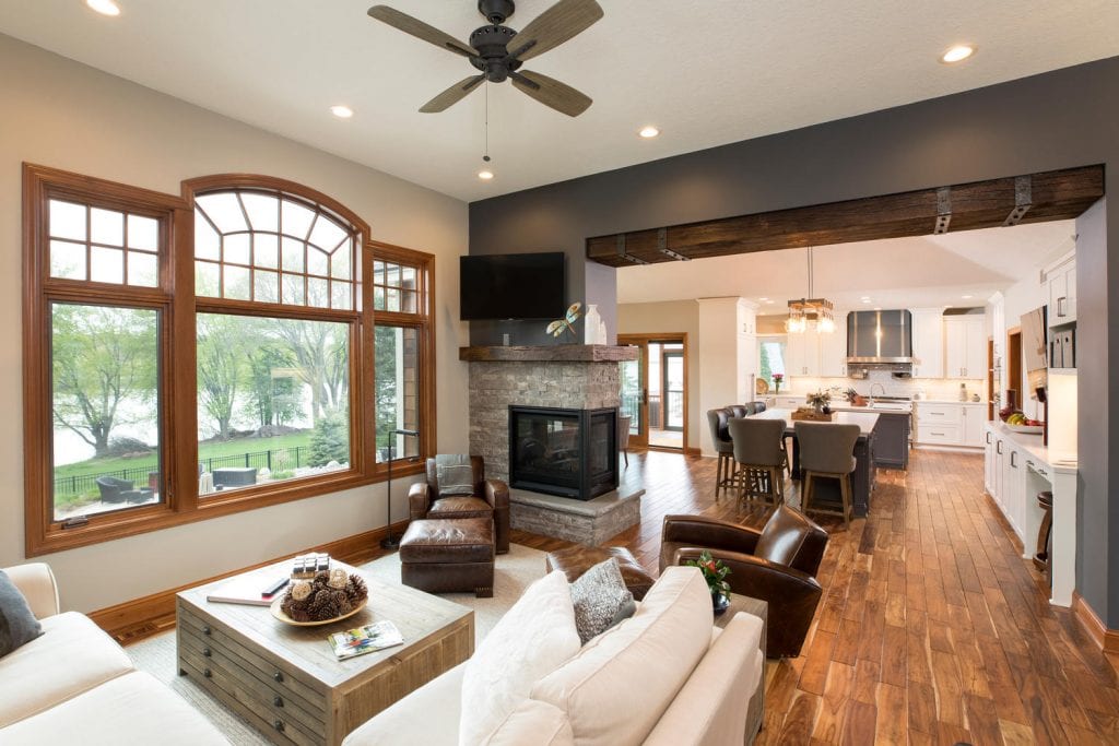 a main level of a house, showcasing a living room with a modern fireplace, wooden floors and a kitchen with white cabinets