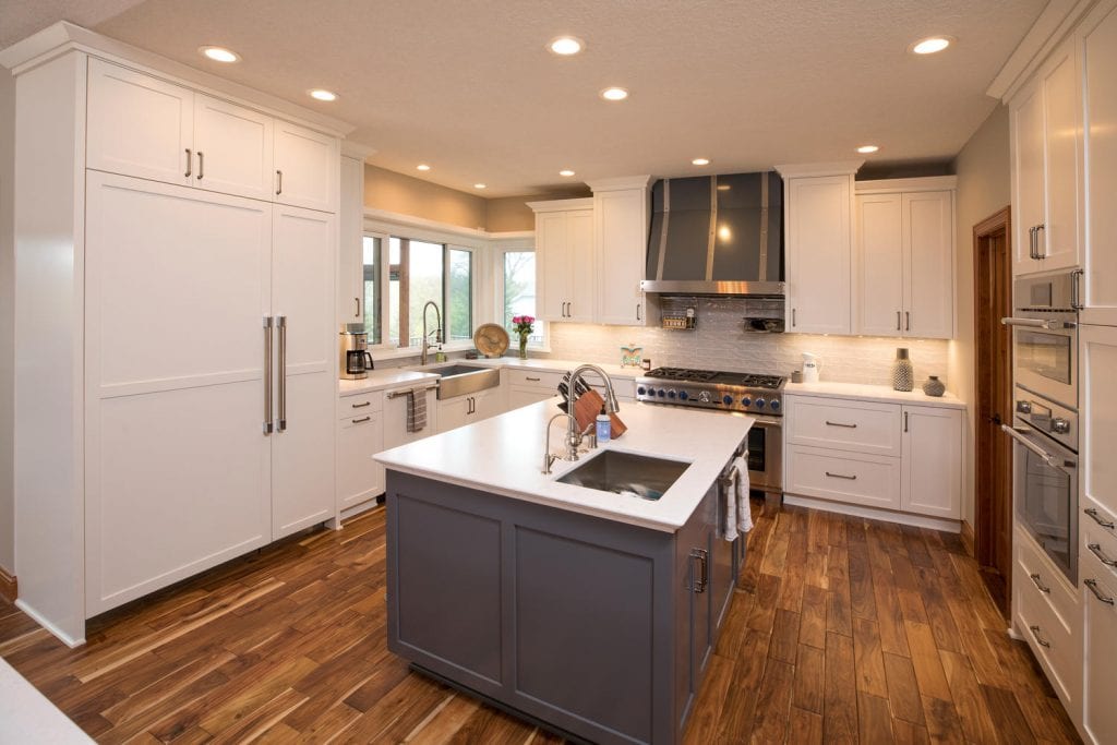 a kitchen with a contrasting island - the cabinets are blue while the countertops are white. the rest of the kitchen cabinets are white.